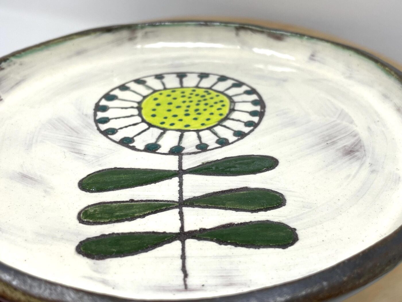 Artisan sunflower plate — deep forest-green leaves on hand-drawn stem — Fabode Ceramics