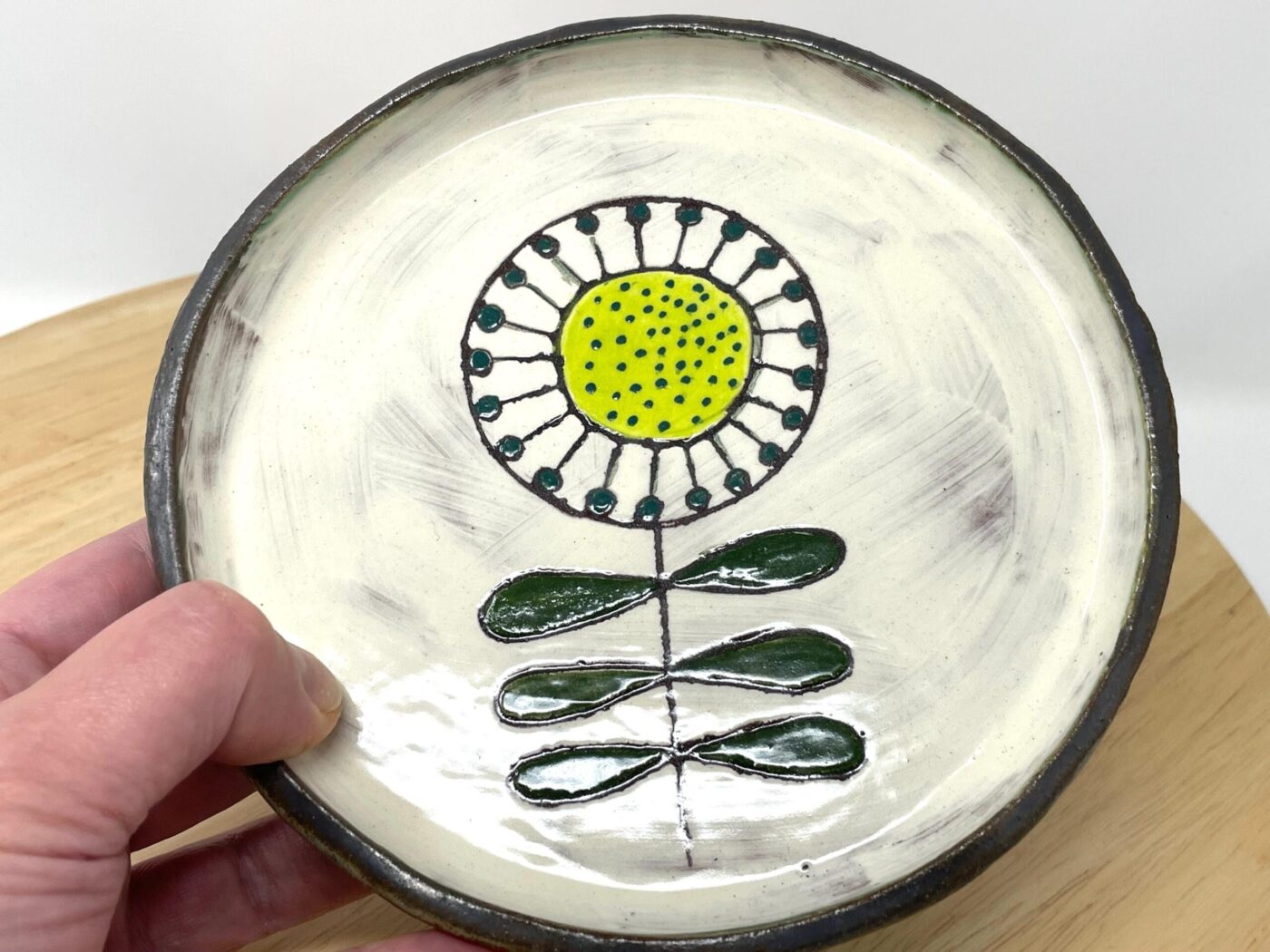 Handmade terracotta plate with sunflower motif — teal-green dots and forest green leaves — Fabode Ceramics