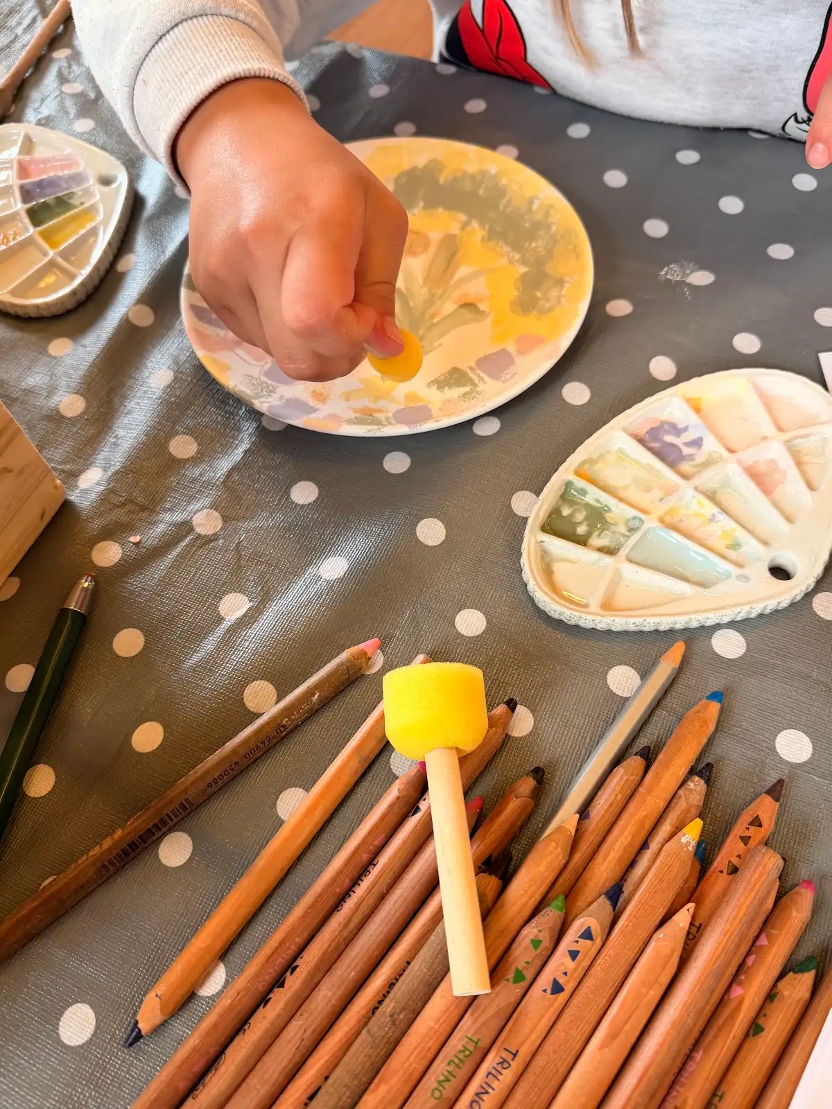 Hands decorating a ceramic plate with sponge painting and pencils at Fabode
