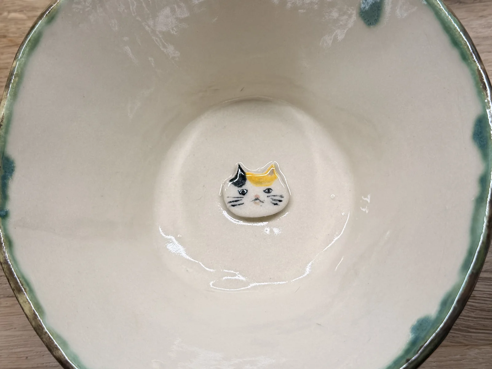 Handmade bowl with a blue-green rim and illustrated centre detail